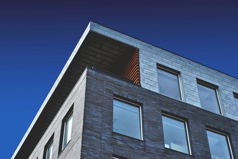 Modernes Gebäude mit flachem Dach und großen Fenstern vor blauem Himmel.
